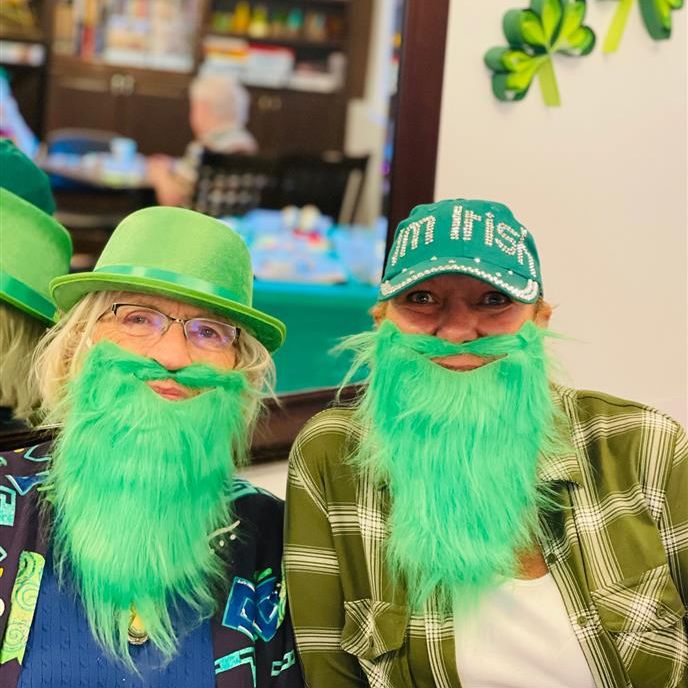 Two women dressed up in St. Patrick's Day gear with large green beards and hats.