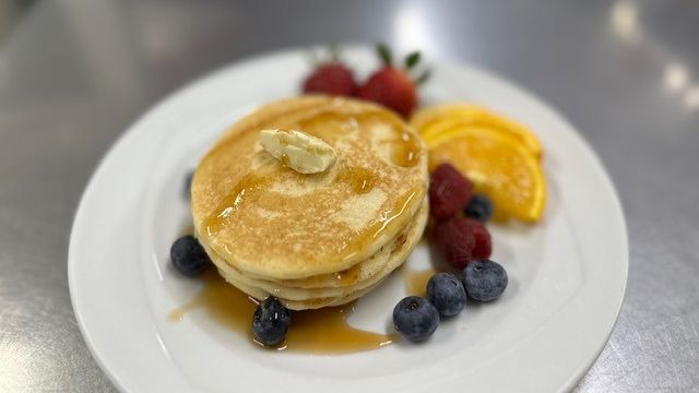 Tasty looking pancakes on a plate with fruit.