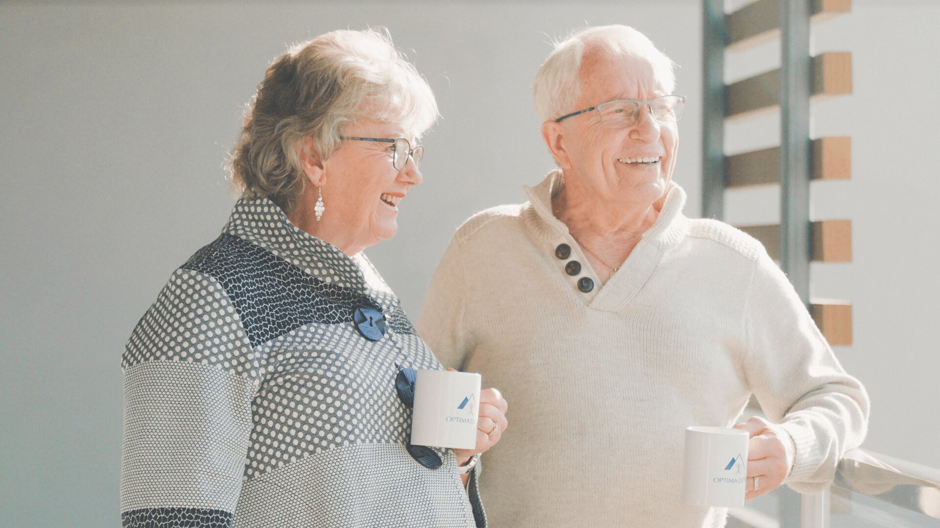 An elderly couple standing at balcony of their senior apartments and enjoying tea