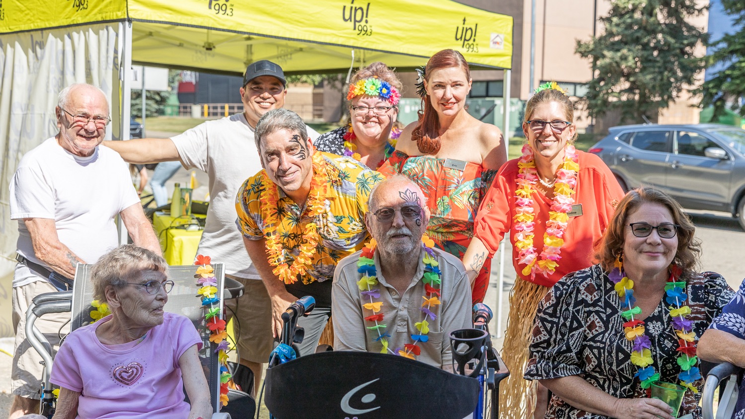 Residents and staff smiling together in their Hawaiian outfits outside a retirement home.