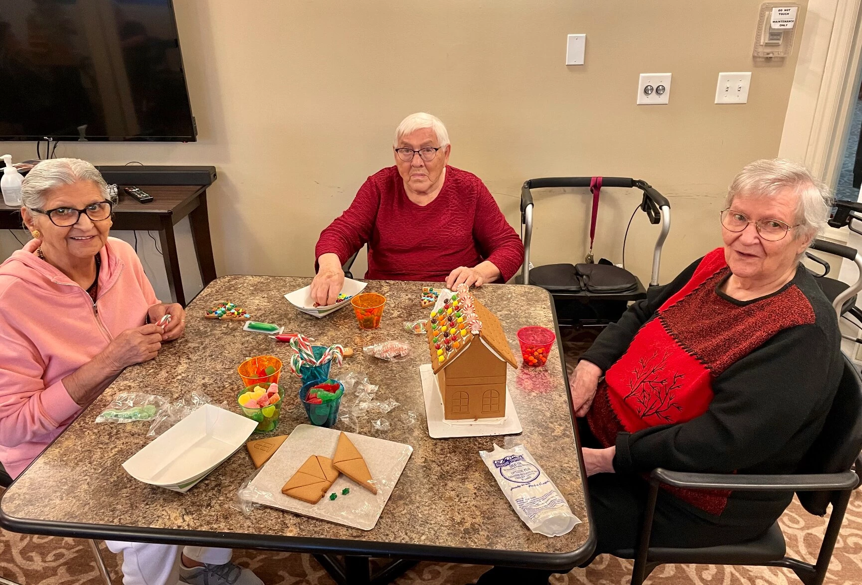 3 elderly women decorating a gingerbread house for Christmas in a senior living community