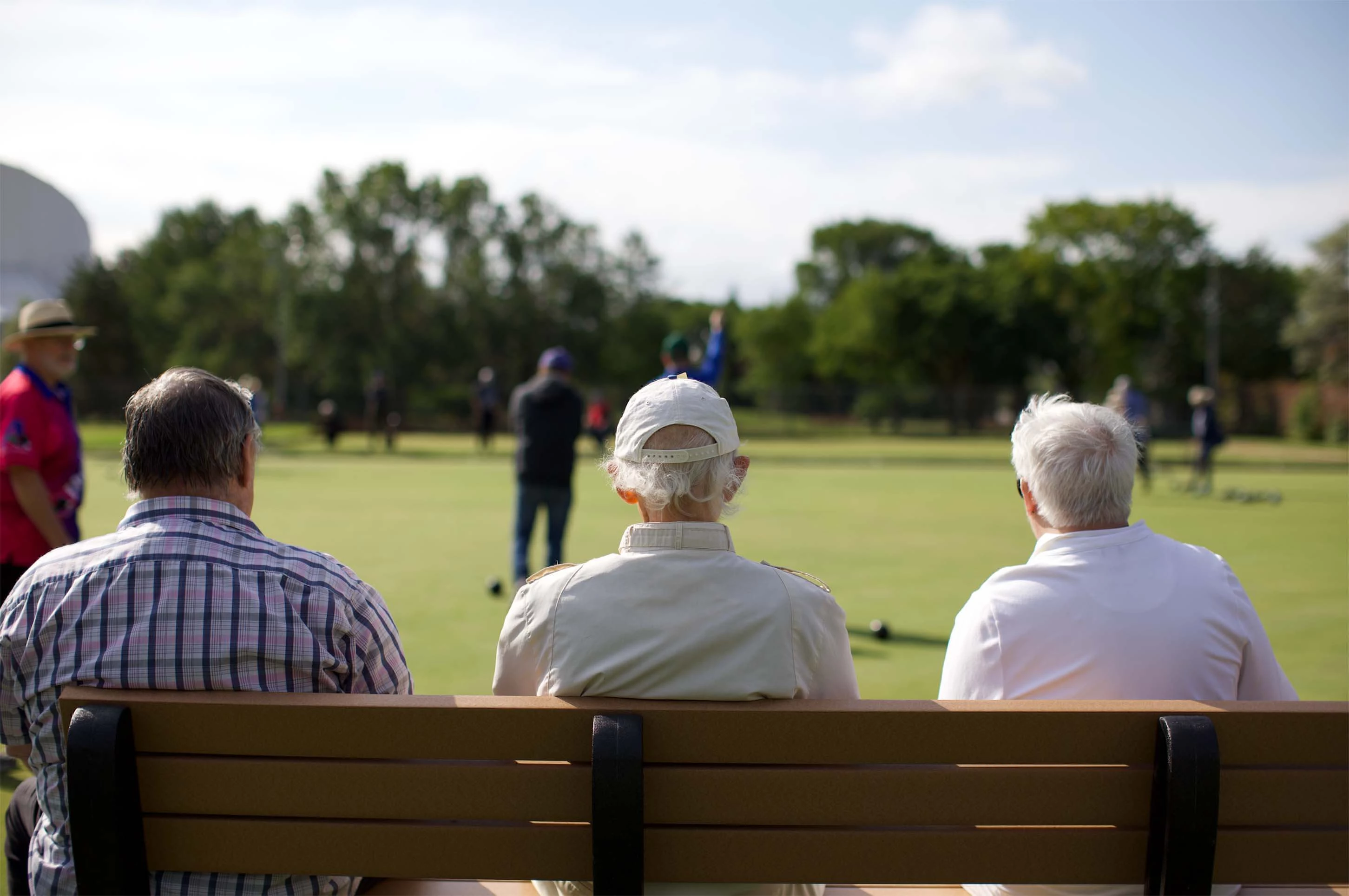 Some senior citizens sitting on a bench in a park doing hobbies for elderly