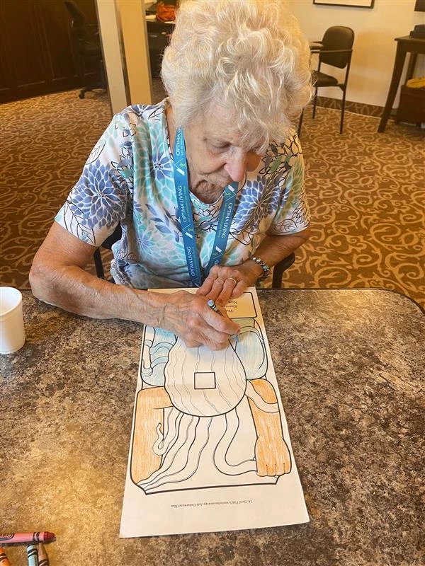 Resident seated and colouring with a blue crayon.