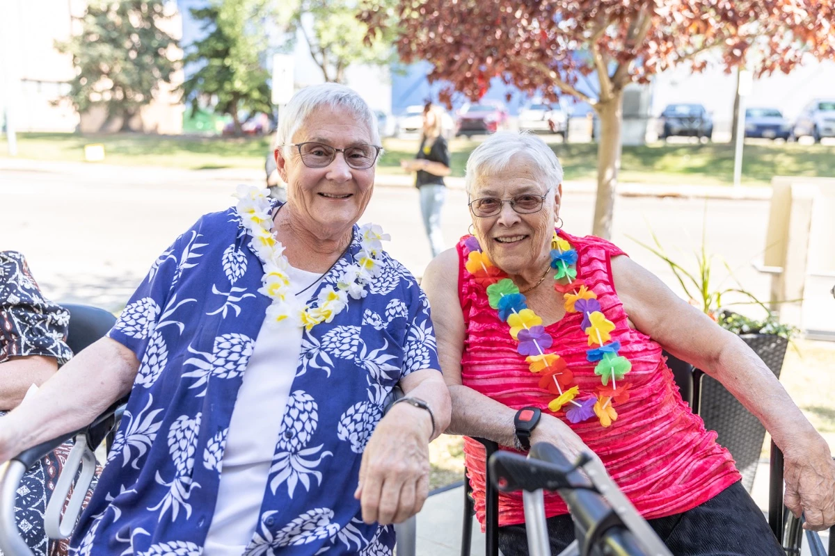 Two residents of a seniors home smiling together and enjoying the nice weather outdoors.